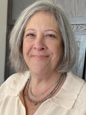 Head and shoulders of Kim Konikow with shoulder-length puffy grey hair and closed smile