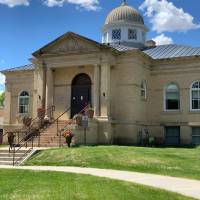 The historic James Memorial (brick) building in Williston with blue skies above and steps leading to green grass