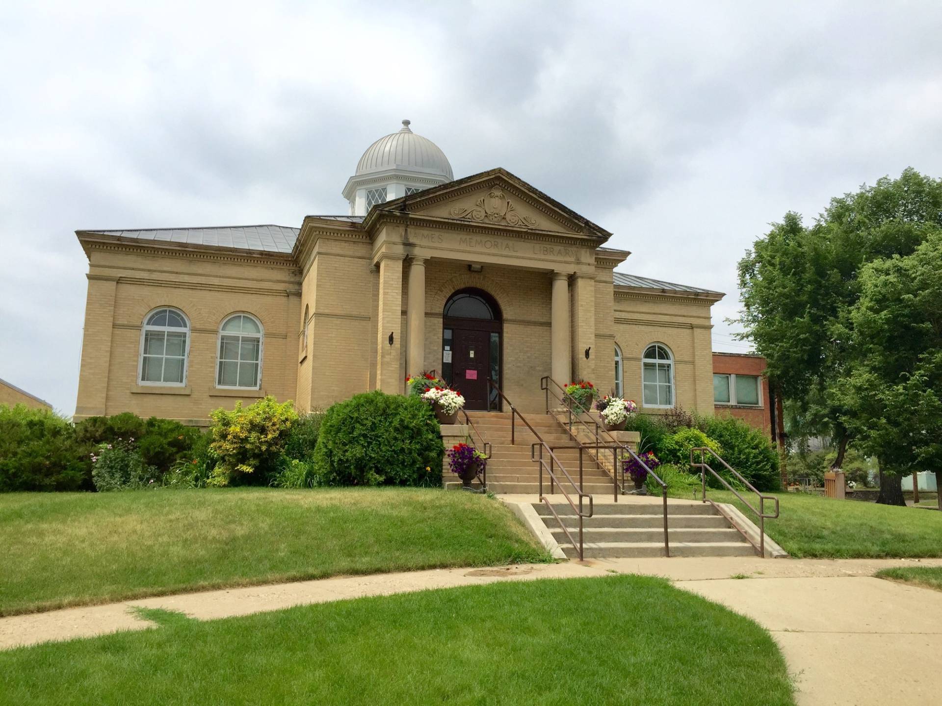 The historic James Memorial (brick) building in Williston with blue skies above and steps leading to green grass