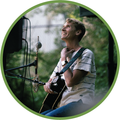 North Dakota Folk Artist Tom Brosseau playing guitar in front of a microphone outside on a summer day
