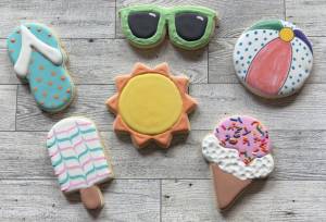 six cookies decorated with a summer theme: a flip-flop, sunglasses, frozen treats, and a beach ball