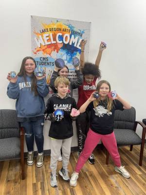 5 middle school students hold up their acrylic paintings on rough cut wood round with big proud smiles 