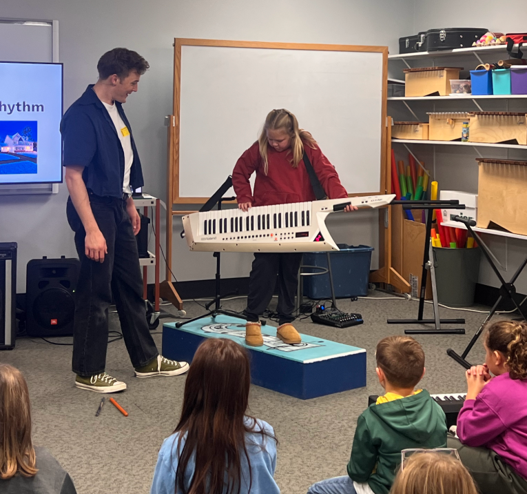 Teaching Artist David Snyder showing a Wyndmere Elementary student how to play a piano guitar with fellow students looking on