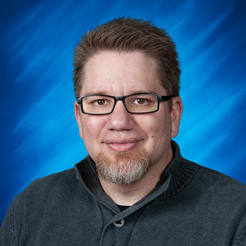 Formal chest-up image of Derek Morin wearing a collared dark-grey sweater with a full-head of dark hair, salt and pepper goatee, dark-rimmed rectangular glasses, light skin and a closed smile