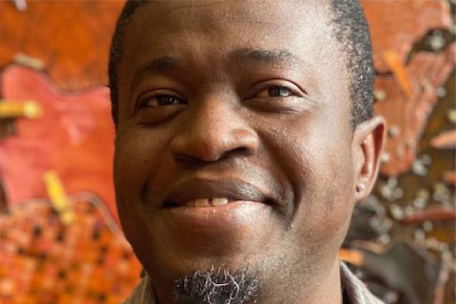 Hamzat Amoussa headshot with slight goatee, tightly shaved hair and a secretive grin