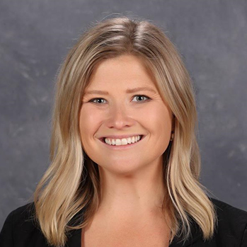 head and shoulders of caucasian Kierstin Hurtt with thick, wavy, shoulder-length blonde hair and a big toothy smile, wearing a black v-neck sweater