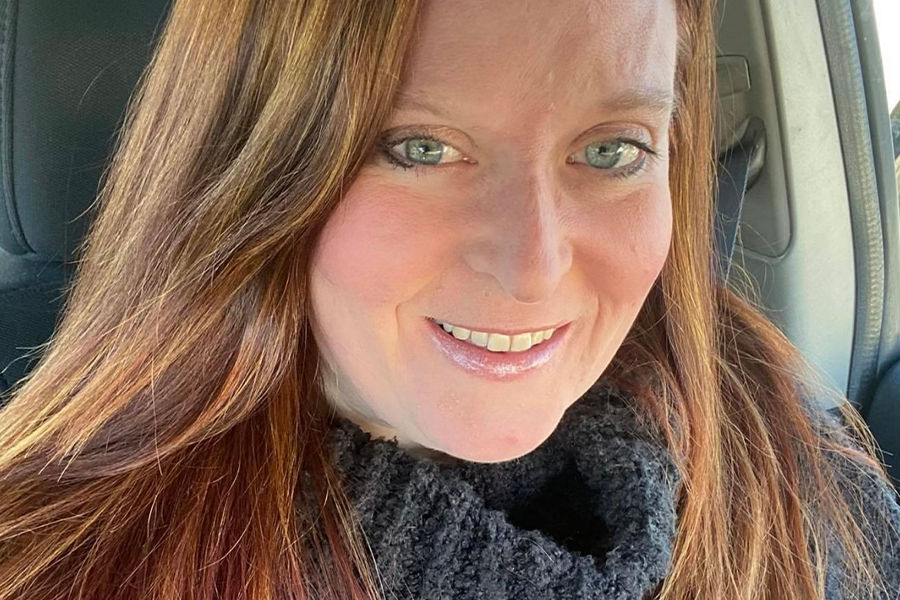 close up face and shoulders of artist Myra Klein with long, straight auburn hair, blue eyes, heavy grey turtle-neck sweater, pale skin, and slightly toothy smile