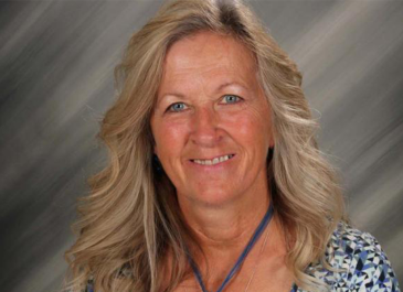 Head and shoulders of Delores Halstead with long wavy blonde hair, wearing large pendant necklace