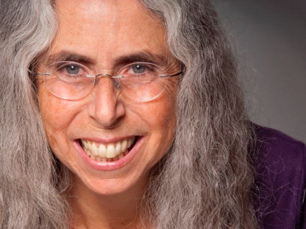 Close-up headshot of Beth Olshansky with big smile, clear glassses and long gray curly hair
