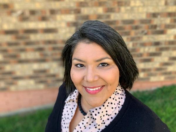 head and shoulders of teaching artist Shelly Sayler with short, straight black hair, wearing a black sweater with a white patterned undershirt, black necklace and toothy smile
