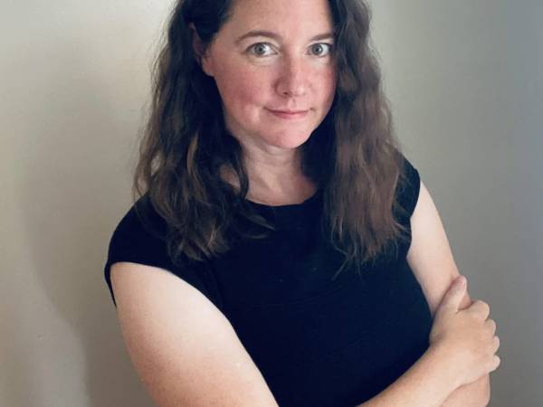 Ali LaRock pictured standing with arms folded across her chest. Wearing a black tee-shirt, with long wavy brown hair down to her shoulders. LaRock smiles slightly as see looks warmly into the camera