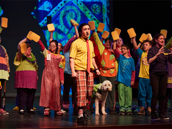 Colorful cast of various races, ages, and abilities in The SpongeBob Musical inhabit the stage in all their glory with neurodiverse SpongeBob and Deaf Patrick Star gesturing grandly with arms open. Photo Credit: Jeff Heimbach