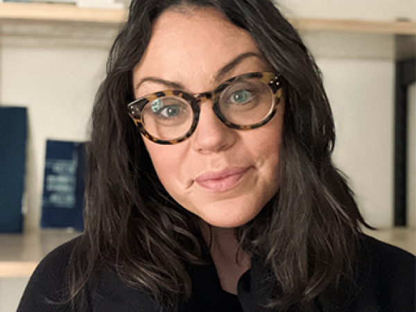head and shoulders of Jessica Christy with long, full, straight dark hair; fair skin; dark shirt; thick, patterned rimmed round glasses; and a closed sweet smile