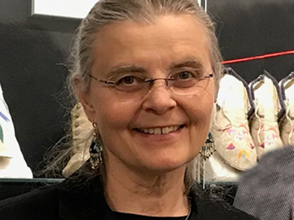 Linda Olson with dirty grey hair pulled back into a ponytail with clear rimmed glasses and a black suit jacket