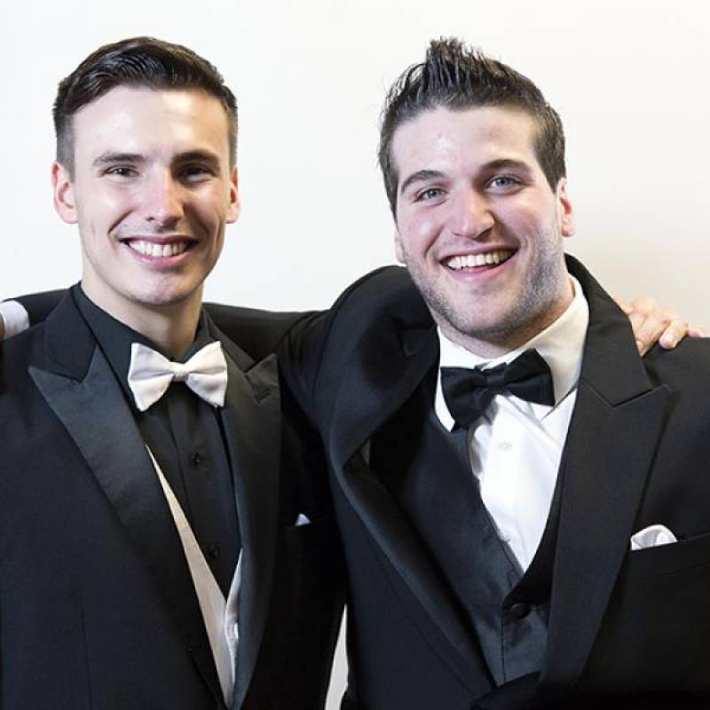 Head & shoulders of Matthew and Eric smiling, wearing black suit jackets with bowties