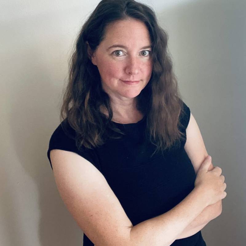 Ali LaRock pictured standing with arms folded across her chest. Wearing a black tee-shirt, with long wavy brown hair down to her shoulders. LaRock smiles slightly as see looks warmly into the camera