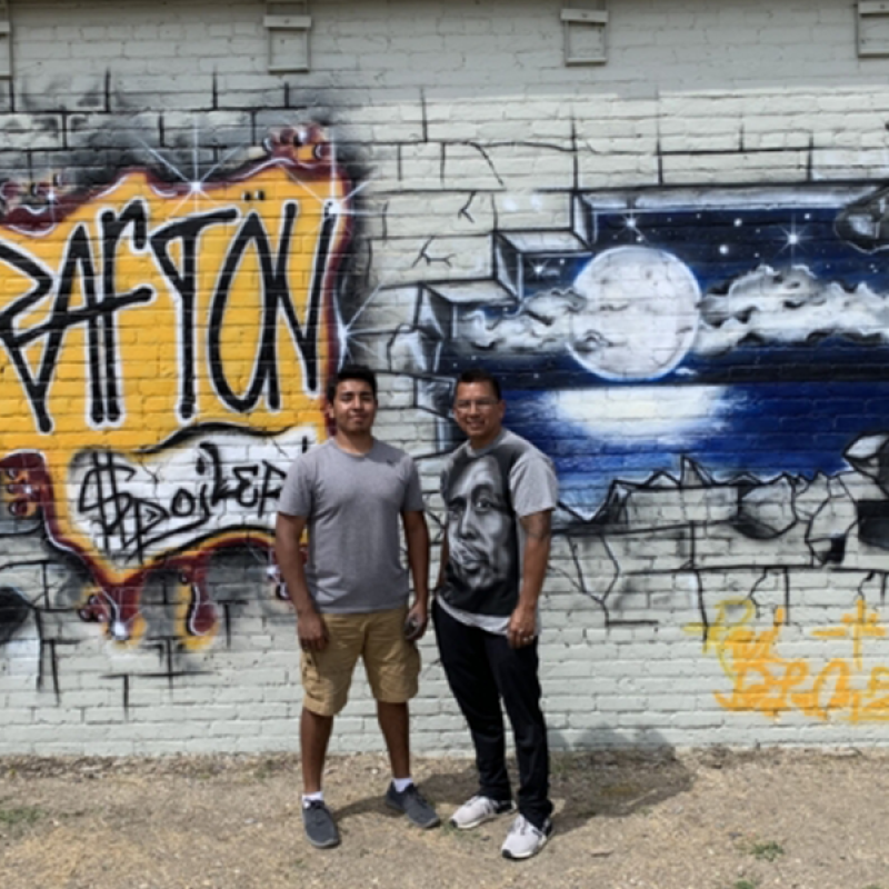2 people standing in front of brick wall grafiti-painted that says Grafton