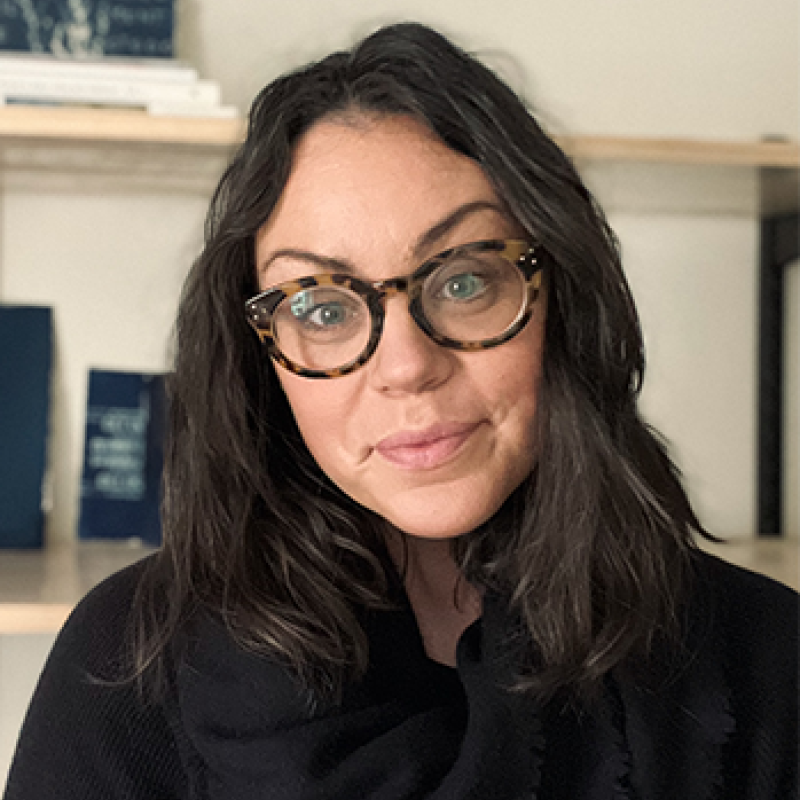 head and shoulders of Jessica Christy with long, full, straight dark hair; fair skin; dark shirt; thick, patterned rimmed round glasses; and a closed sweet smile