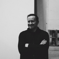 waste-up black and white photo of artist James Culleton wearing a black long-sleeve shirt with short dark hair and a closed smile