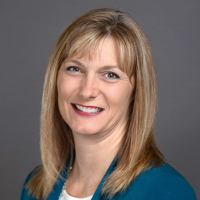Head and shoulders of straight blonde-haired, brown-eyed Christi Stonecipher wearing teal jacket over white shirt on gray background