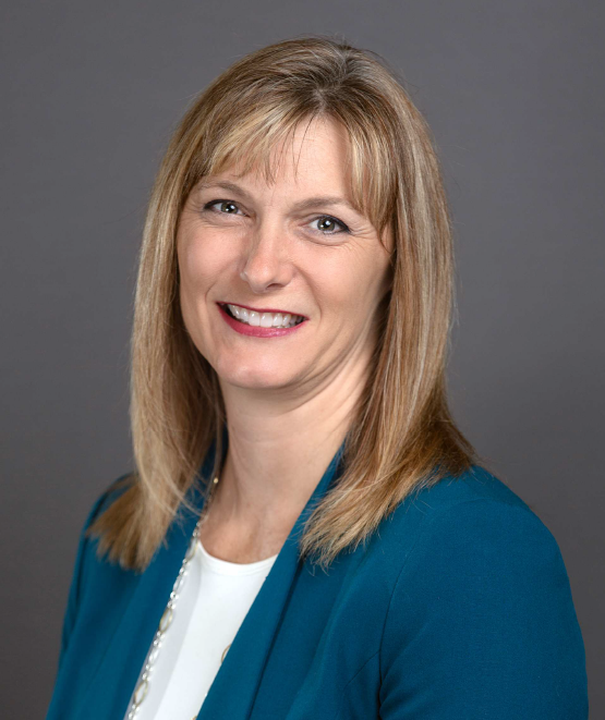 Head and shoulders of straight blonde-haired, brown-eyed Christi Stonecipher wearing teal jacket over white shirt on gray background