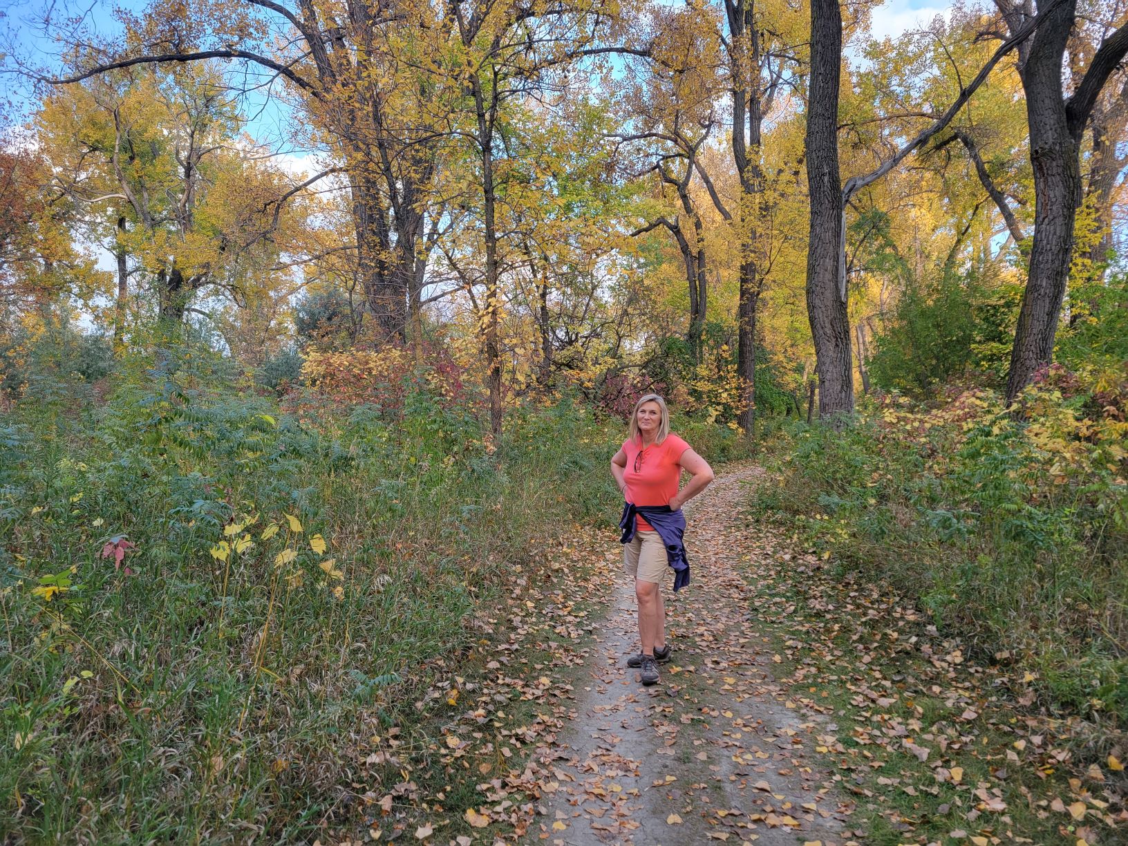 Christi Stonecipher, wearing shorts, standing on a paved trail on a fall day with grass and trees all around.