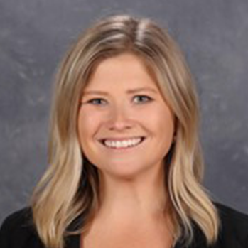 head and shoulders of caucasian Kierstin Hurtt with thick, wavy, shoulder-length blonde hair and a big toothy smile, wearing a black v-neck sweater