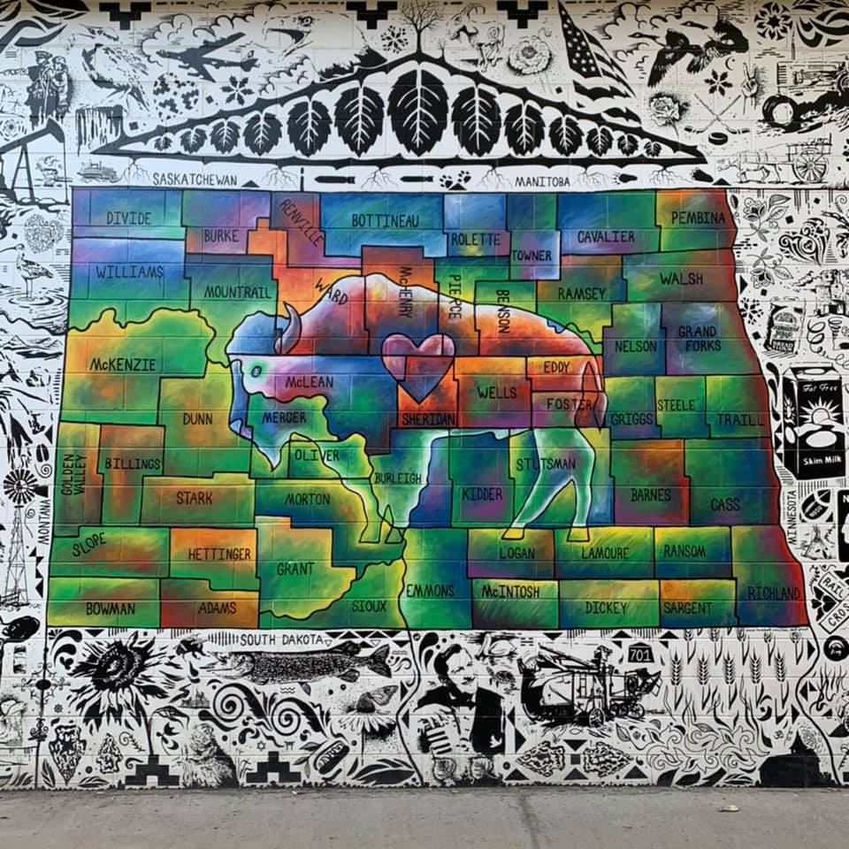 Photo of a mural painted by Paul Noot. It is a colorful painting that shows all of the counties of North Dakota, a buffalo and a heart in the middle of the mural.
