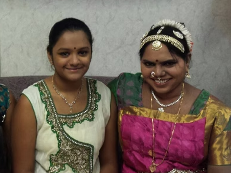 Indian dance instructor Margreat Sam sitting with one of her students, both smiling and in full regalia