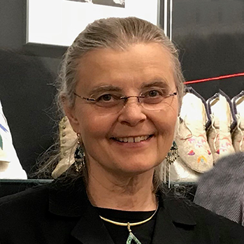 Linda Olson with dirty grey hair pulled back into a ponytail with clear rimmed glasses and a black suit jacket