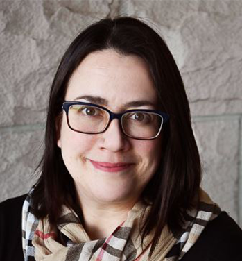 Head and Shoulders of Robin Bosch with shoulder-length straight dark hair, dark-rimmed glasses, light skin, dark eyes, and closed smile wearing a black shirt with a flannel-patterned scarf