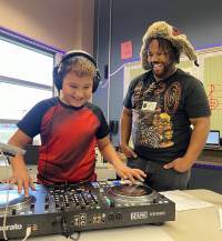 Arts in Education program with a student from Bennett Elementary in Fargo laughing while he is playing with a DJ's turn table while a teacher looks on