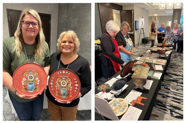 Two women holding painted plates, an exhibit of Norwegian painted items on a table