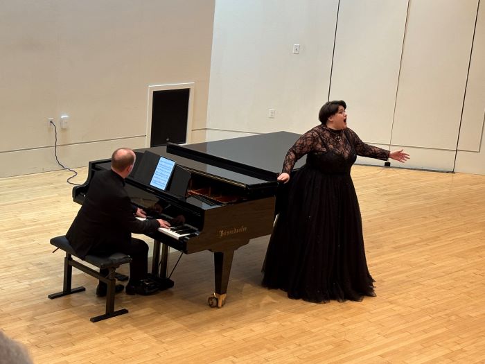 A man plays piano, a woman in a black dress sings beside piano