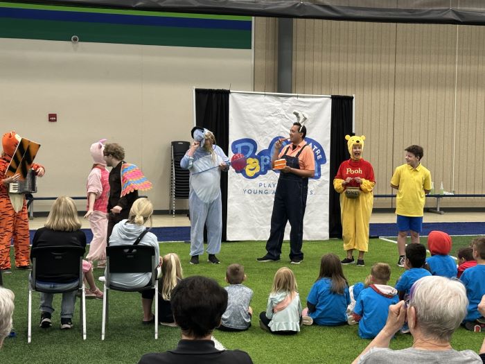 Children and adults sit and watch performers dressed as animals