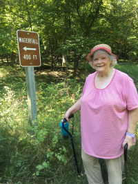 Mary Lizakowski standing next to a waterfall trailhead in a wooded area of North Dakota