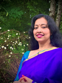 Aparupa Chatterjee with shoulder-length dark hair, dot on her forehead and nice smile, wearing a traditional blue and teal Indian saris