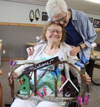 Lollie Addair hugs her friend and Maryhill Manor resident Bonnie Daub, shown holding artwork   