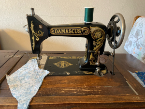 Black treadle sewing machine with Damascus logo, sitting on top of wooden cabinet