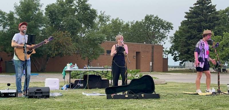 3 people singing and playing guitars on a grassy lawn