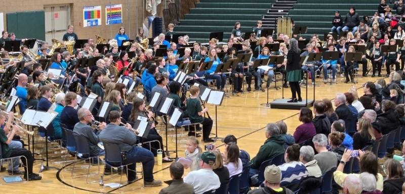 Large adult band playing in front of a large audience in middle school gym