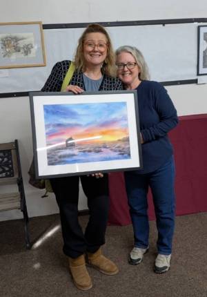 two women standing behind and holding a framed piece of landscape artwork