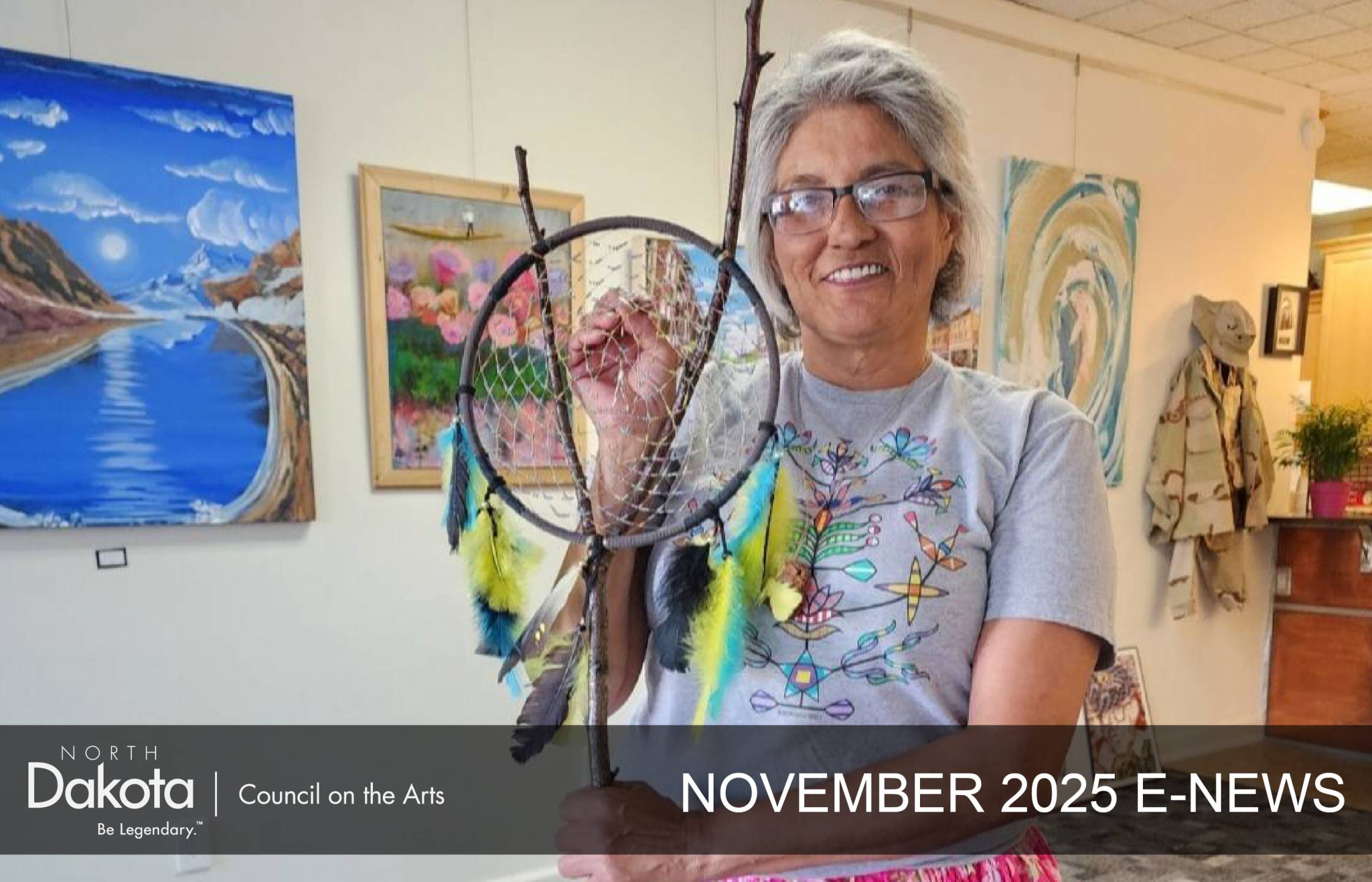 A smiling woman in a gray t-shirt holds a handmade dreamcatcher with colorful feathers in North Dakota.