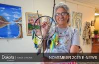 A smiling woman in a gray t-shirt holds a handmade dreamcatcher with colorful feathers in North Dakota.