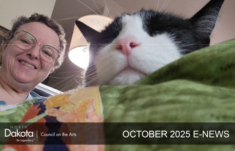 Fiber artist Jane Gaffrey carefully affixes a label to her latest quilt, "Nanna’s Daffodils" while Norman, a feline companion, is eager to assist.