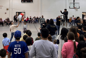 A school gym filled with mostly Hispanic people of all ages participating in La Posada, a Christmas celebration, Watford City 2021