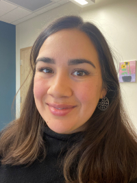 Yolanda Rojas with long, straight dark hair, dark eyes, dangling earrings, with partially closed smile, wearing black turtle-neck