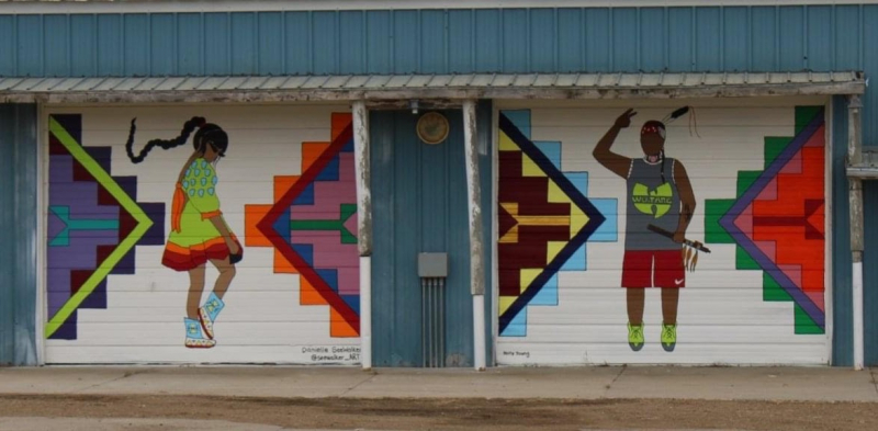 Outdoor painted mural showing a Native girl and Native boy and colorful Native shapes by Dakota artist Holly Young