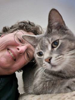 North Dakota artist Jane Gaffrey smiling and posing for a selfie with her gray tabby cat, Stormy.