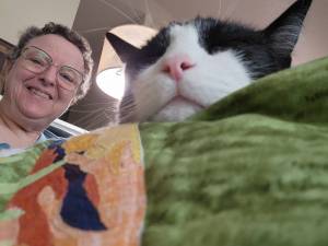 Jane Gaffrey carefully affixes a label to her latest quilt, Nanna’s Daffodils. Norman, a feline companion, is eager to assist